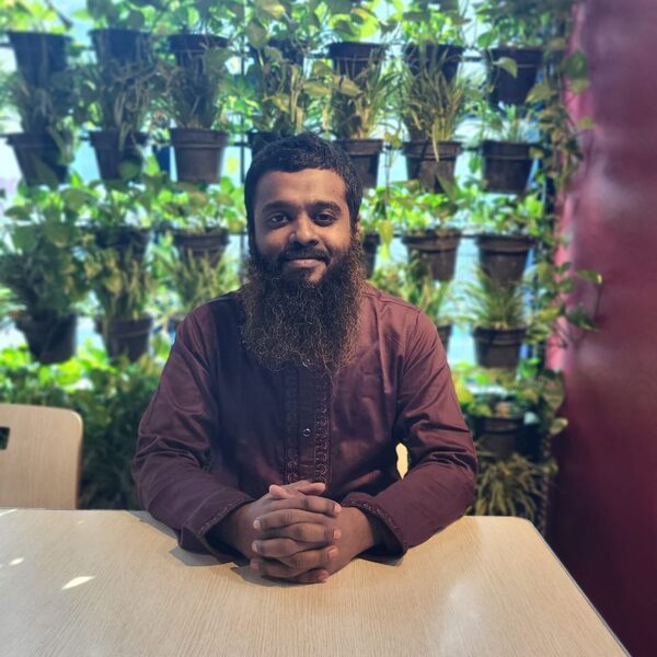 Portrait of Sk. Kamruzzaman seated at a table in front of a living plant wall